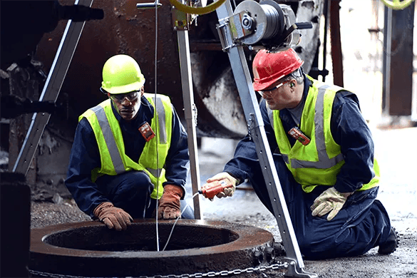 Two workers using confined space monitors to test a confined space